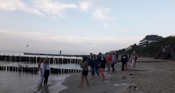 Grupa dzieci i opiekunów spaceruje po plaży mocząc swoje stopy w morzu