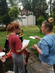 pani-pedagog-rozdaje-dzieciom-siedzacym-przy-stole-na-swiezym-powietrzu-dyplomy-z-nagrodami.jpg
