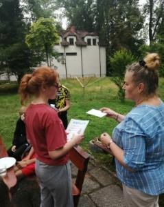 pani-pedagog-rozdaje-dzieciom-siedzacym-przy-stole-na-swiezym-powietrzu-dyplomy-z-nagrodami.jpg