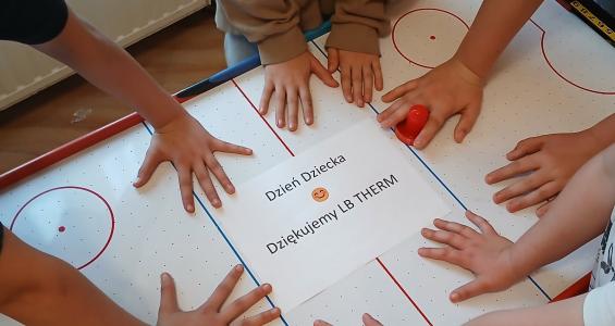 zdjęcie - 4 pary dzięciecych rąk dotyka kartki na której jest napis Dzień Dziecka.jpg